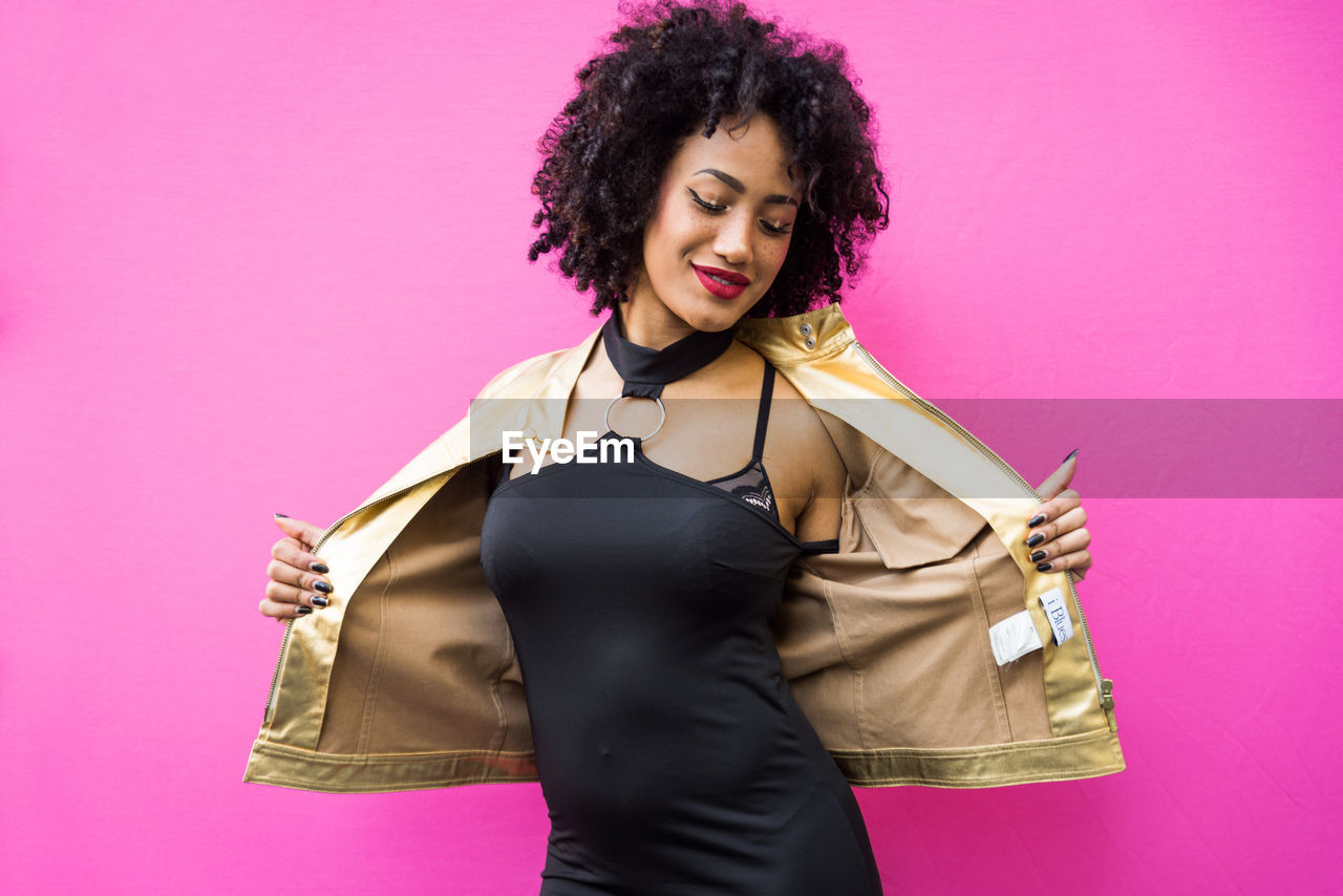 Fashionable young woman with curly hair against pink background