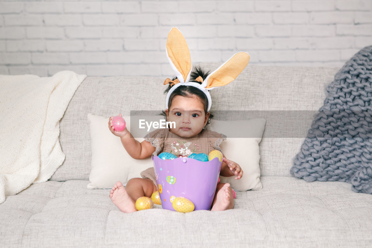 Portrait of cute baby girl sitting on sofa at home