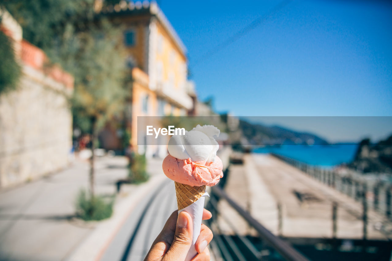 Cropped hand holding ice cream cone against clear blue sky