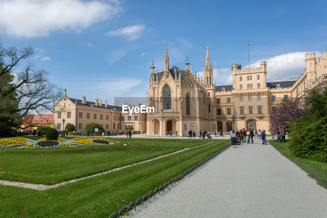 architecture, built structure, building exterior, sky, travel destinations, château, estate, stately home, travel, history, the past, nature, city, tourism, plant, building, grass, cloud, palace, group of people, tree, blue, town square, garden, castle, tourist, mansion, religion, neighbourhood, landmark, outdoors, day, formal garden, place of worship, facade, lawn, holiday, men, government