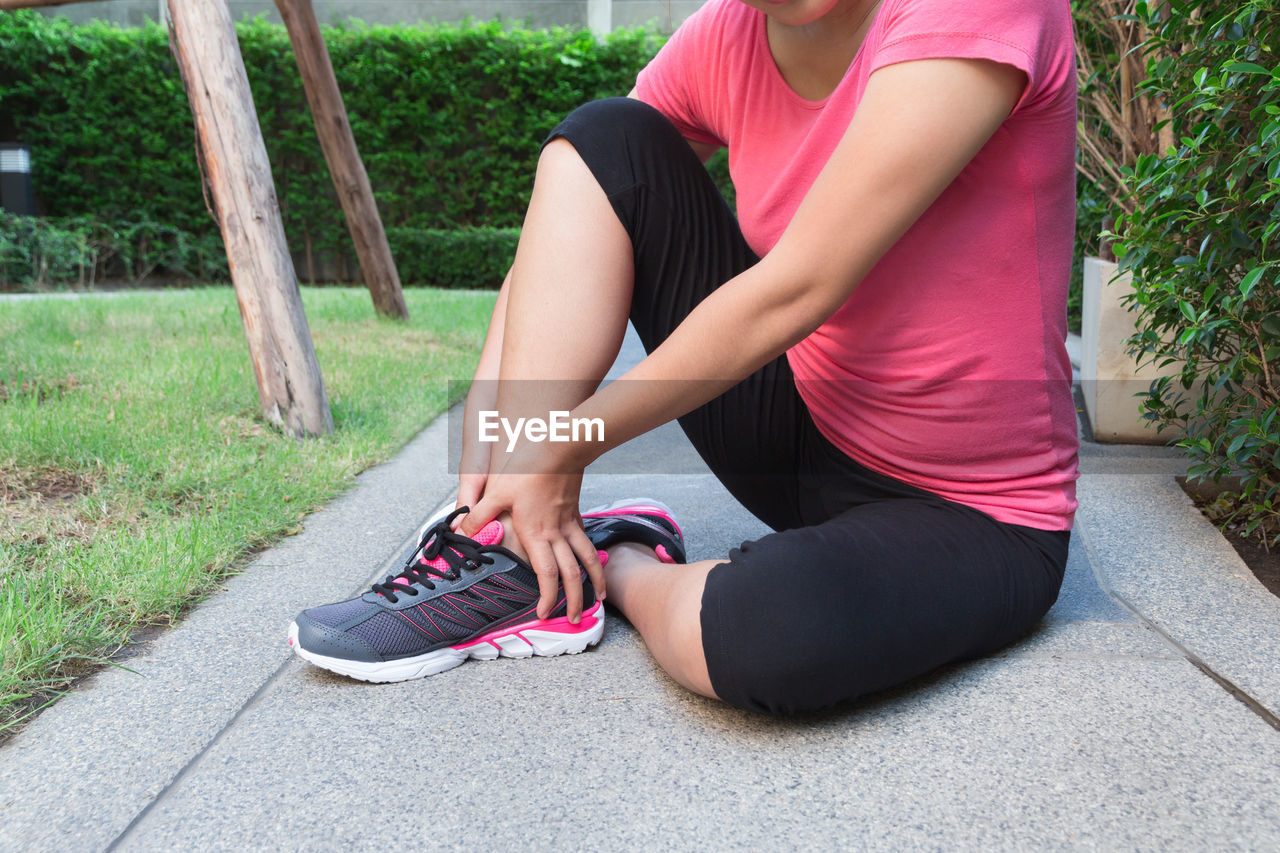 Low section of woman wearing shoes on footpath