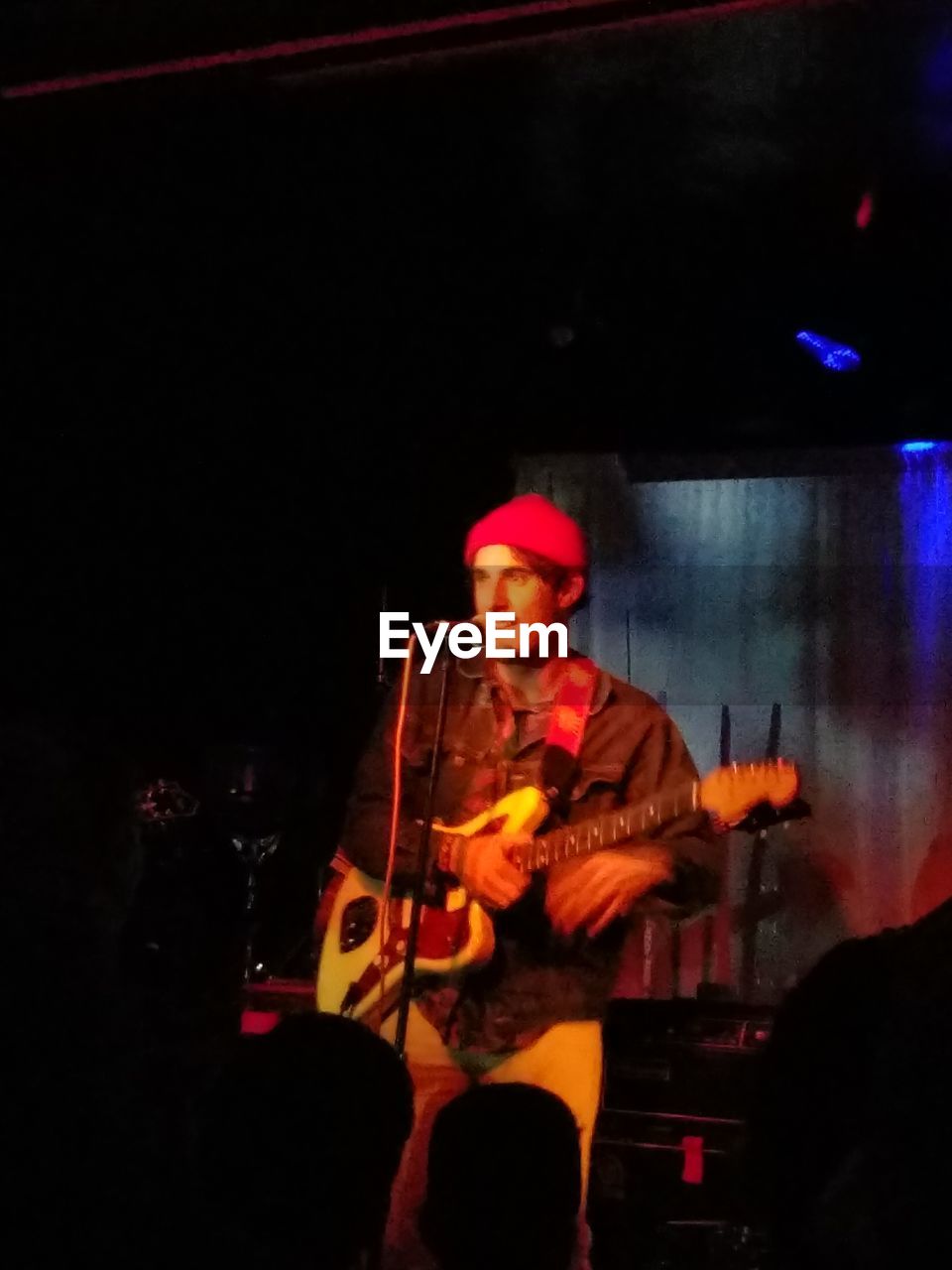 FULL LENGTH OF MAN PLAYING GUITAR AT ILLUMINATED NIGHTCLUB