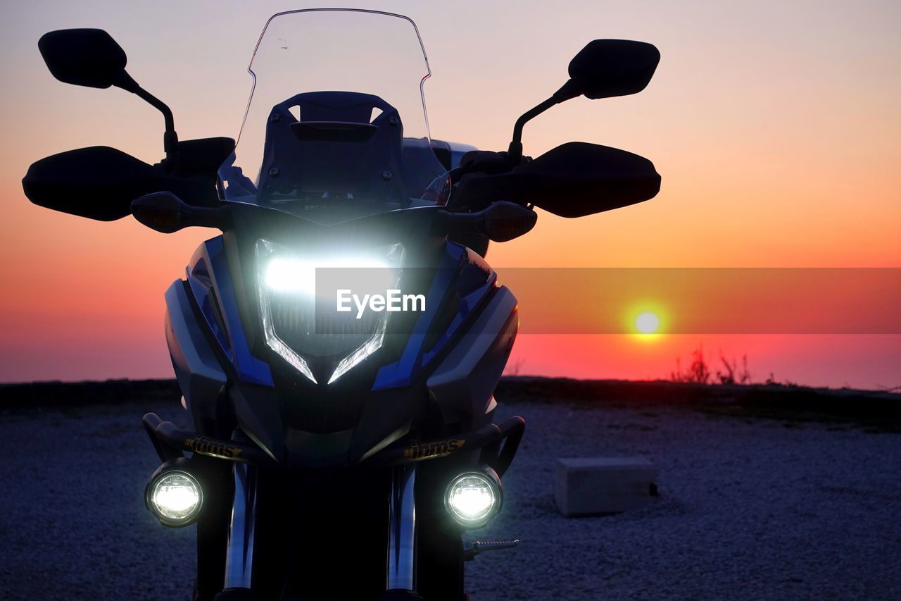 Motorcycle parked on land against sky during sunset