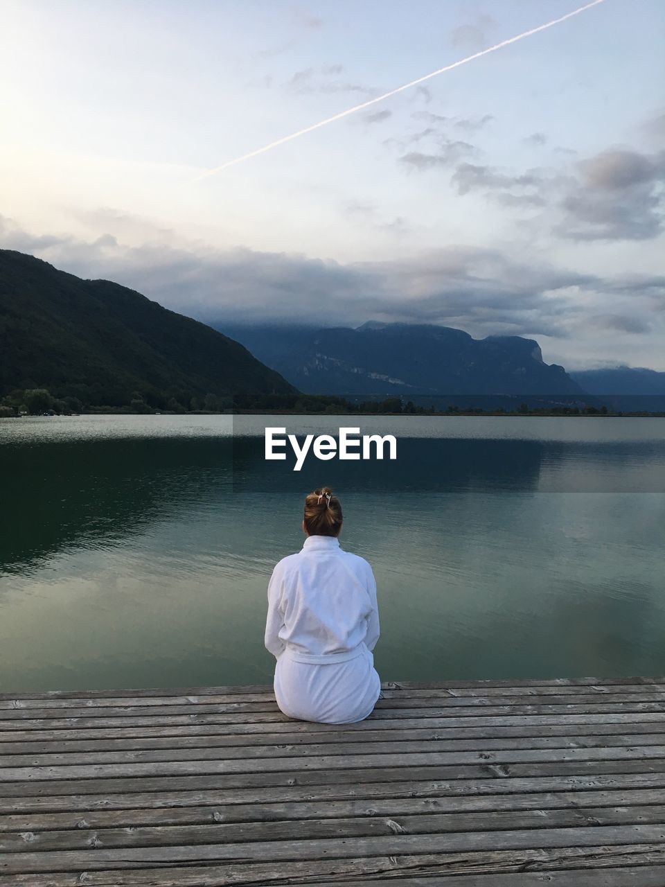 Rear view of woman sitting on pier over lake