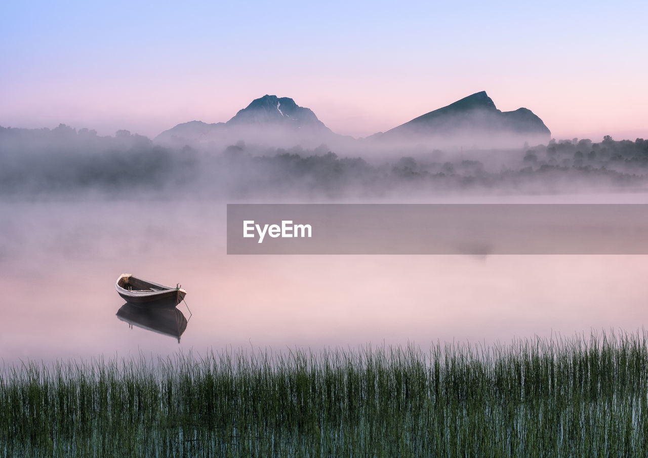 Scenic view of field by lake against sky during sunset