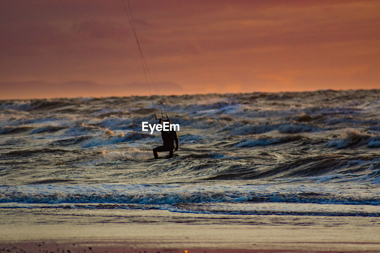 Silhouette man surfing in sea against sky during sunset