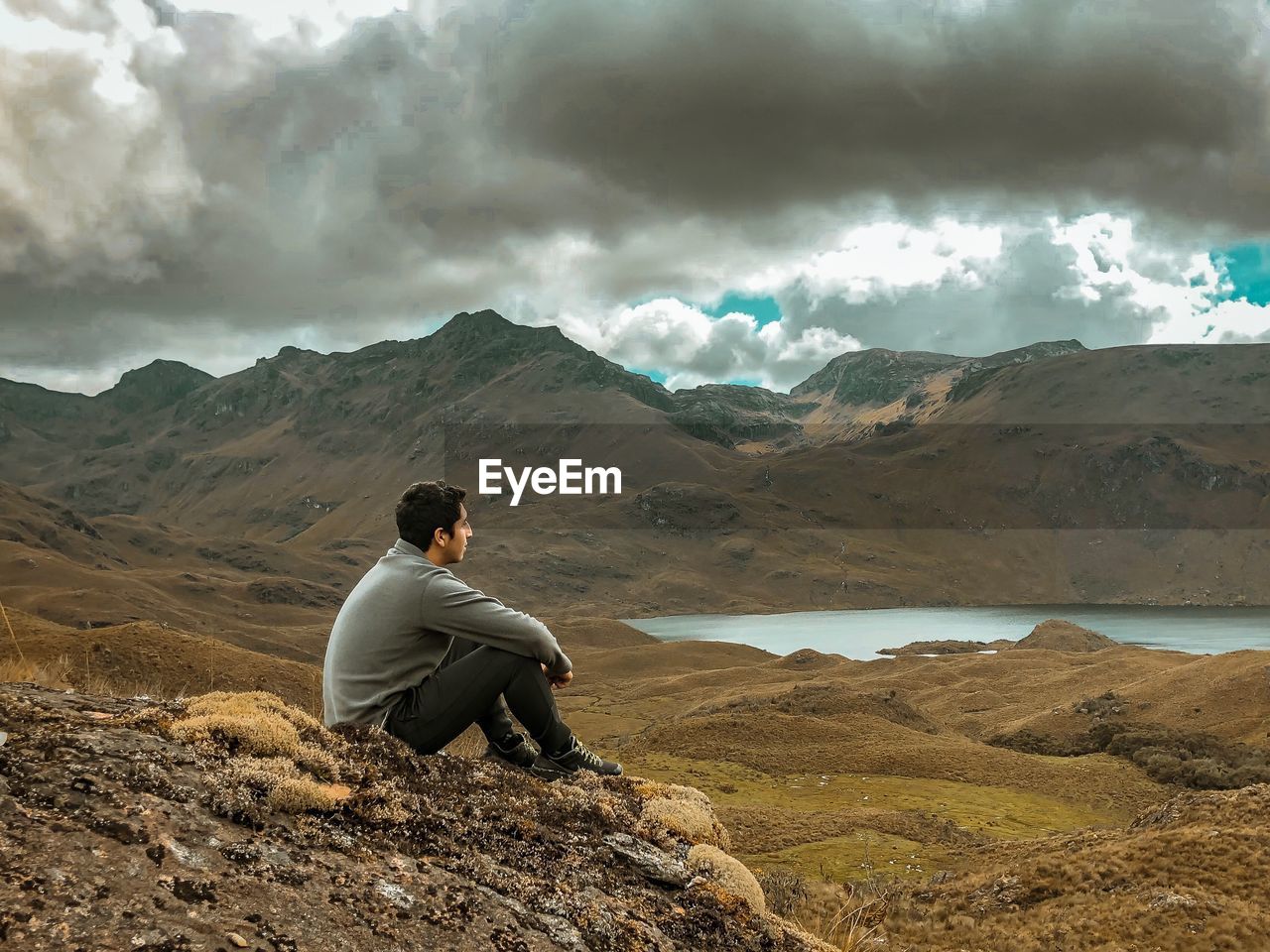 Full length of man sitting on cliff against sky