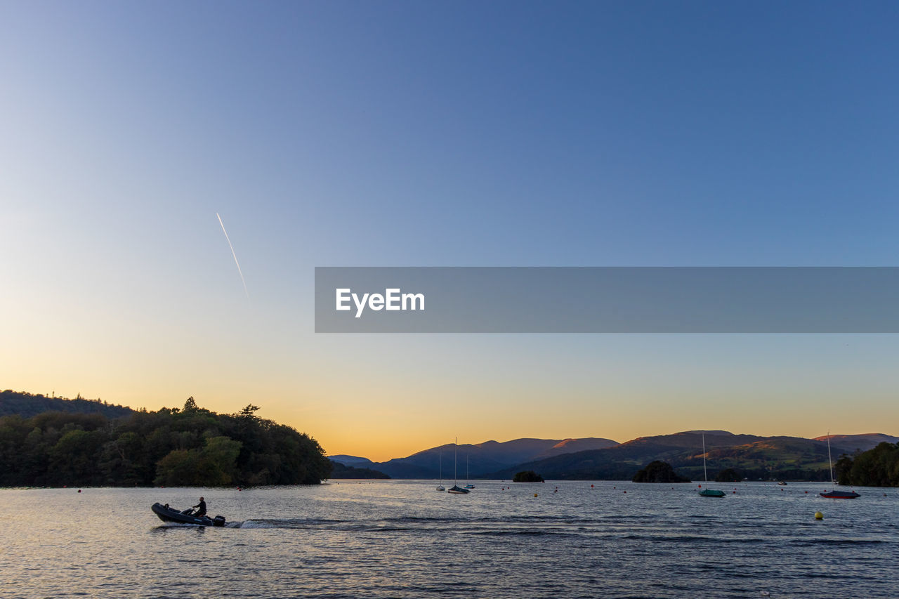 SILHOUETTE BOATS ON SEA AGAINST CLEAR SKY DURING SUNSET