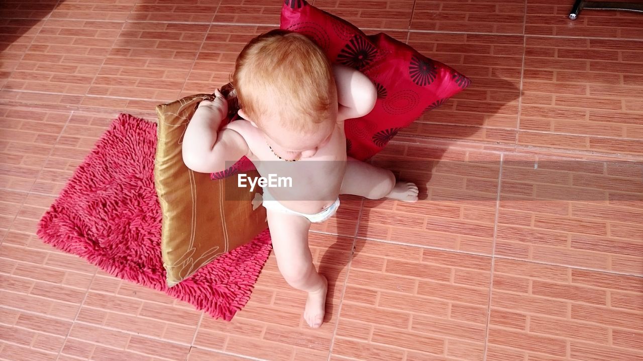 High angle view of baby girl holding cushions and standing on floor