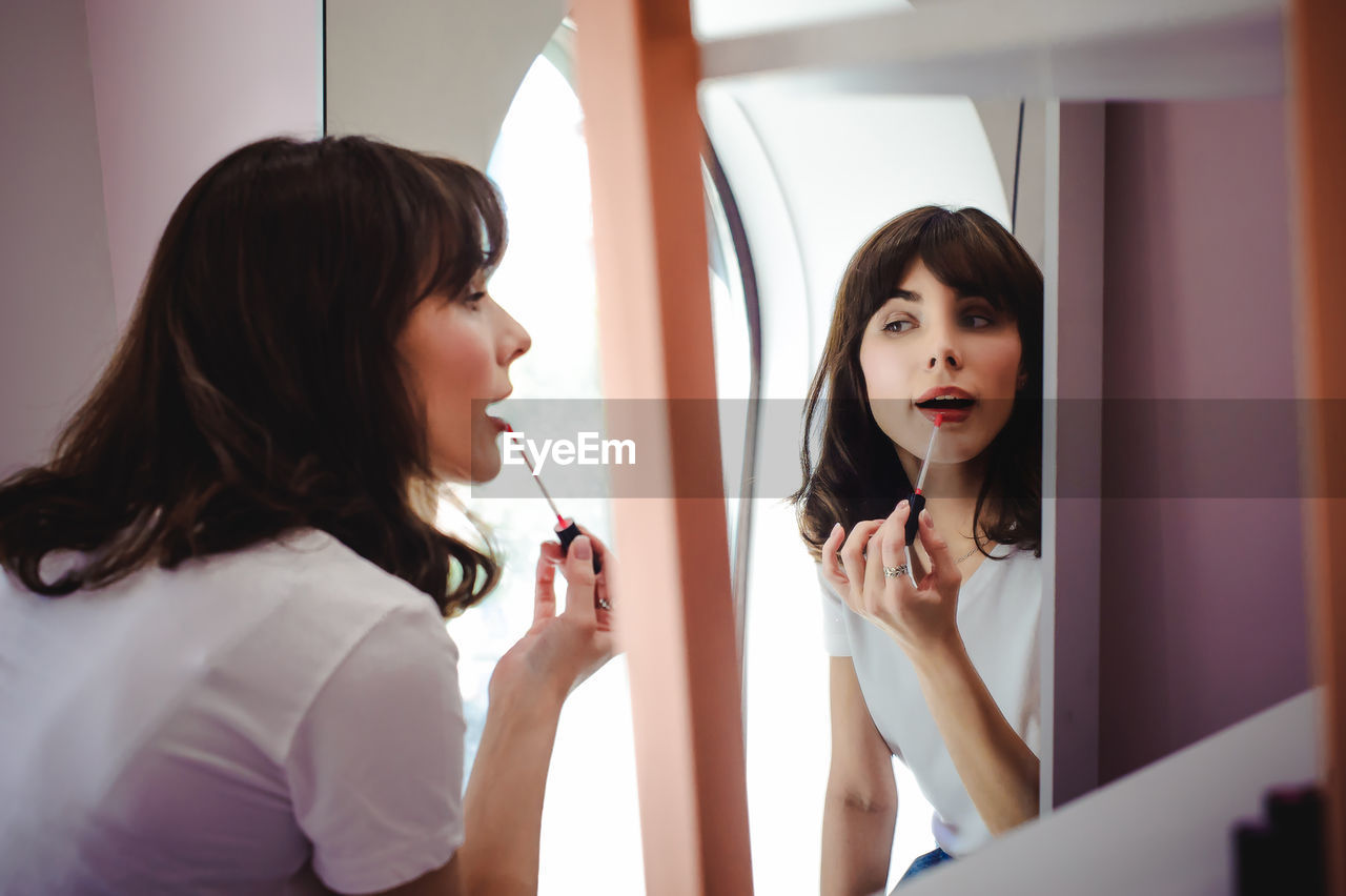 Close-up of young woman applying red lipstick in front of mirror at home