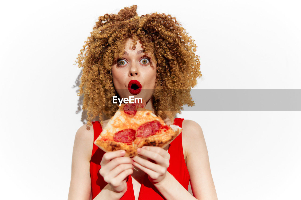 fast food, curly hair, one person, white background, studio shot, human hair, portrait, women, food, food and drink, young adult, adult, person, unhealthy eating, hairstyle, eating, indoors, clothing, human face, afro, looking at camera, baked, holding, human mouth, cut out, red, biting, mouth open, emotion, snack, surprise, copy space, female, headshot, front view, facial expression, performing arts