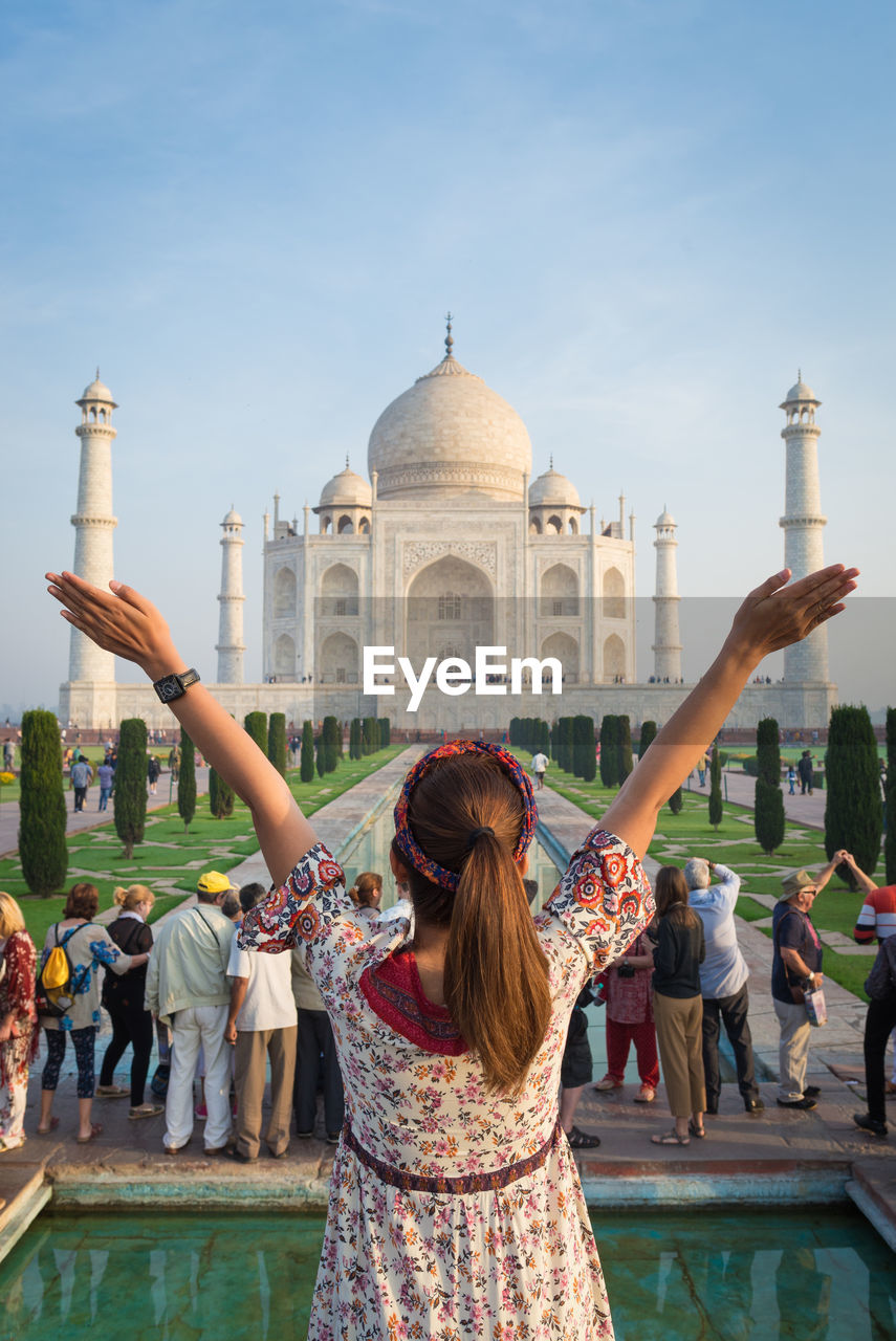 Girl with arms raised standing against taj mahal