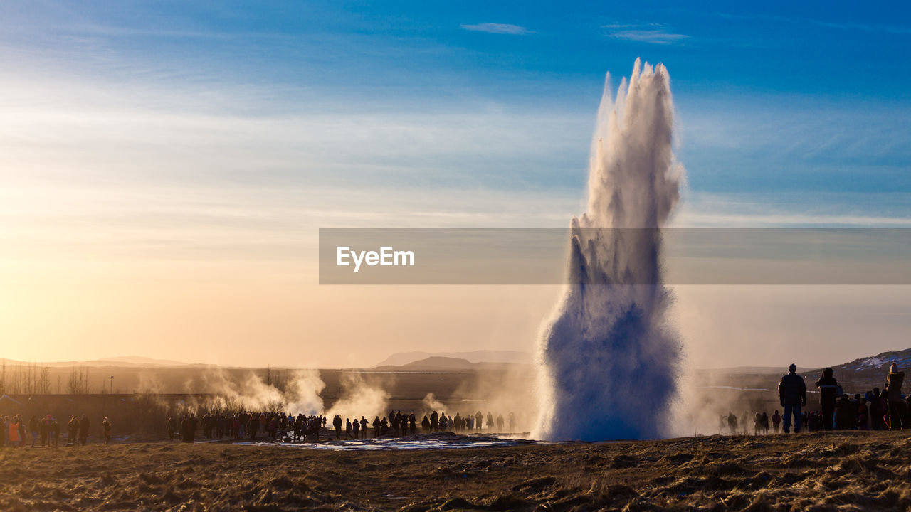 People standing by geyser on field against sky