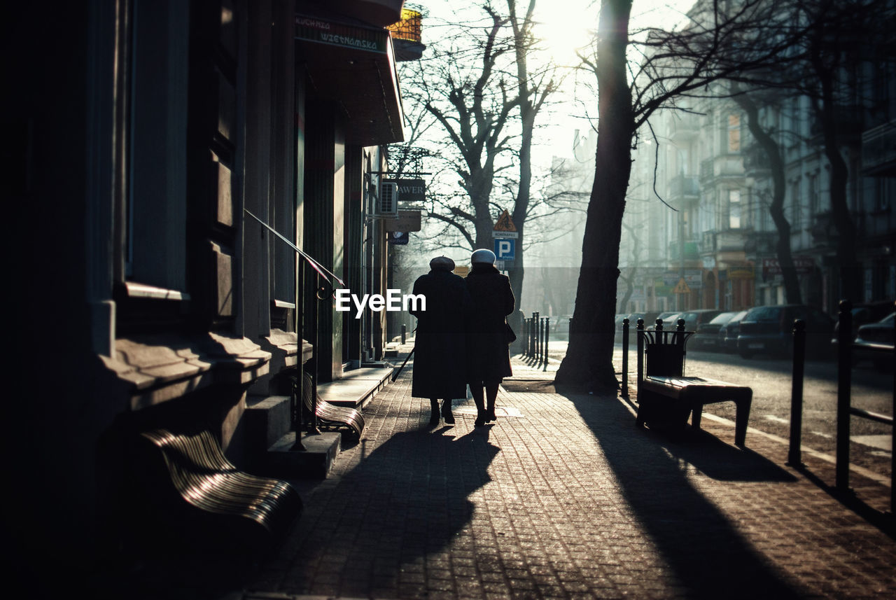 Rear view of people walking on sidewalk in city