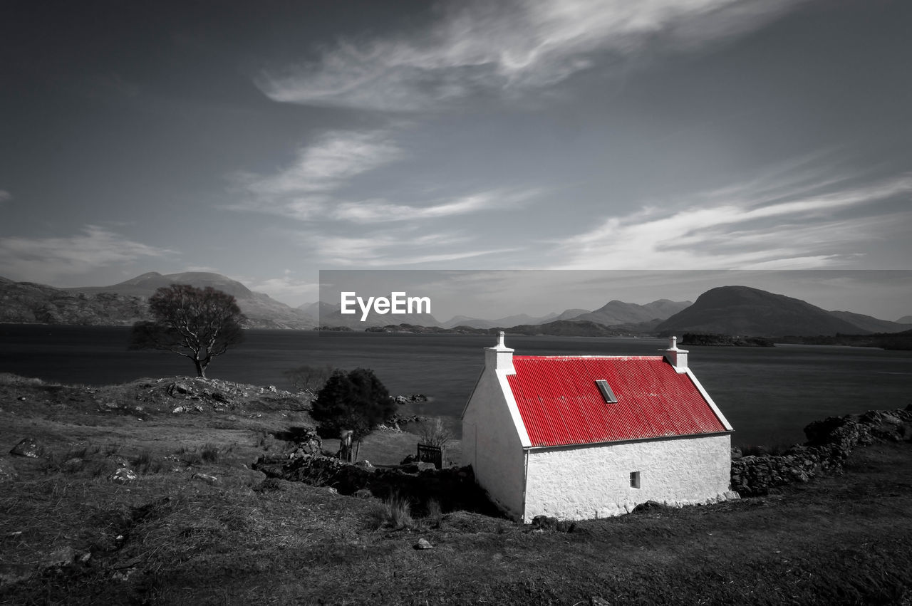 View of lone house on riverbank against cloudy sky