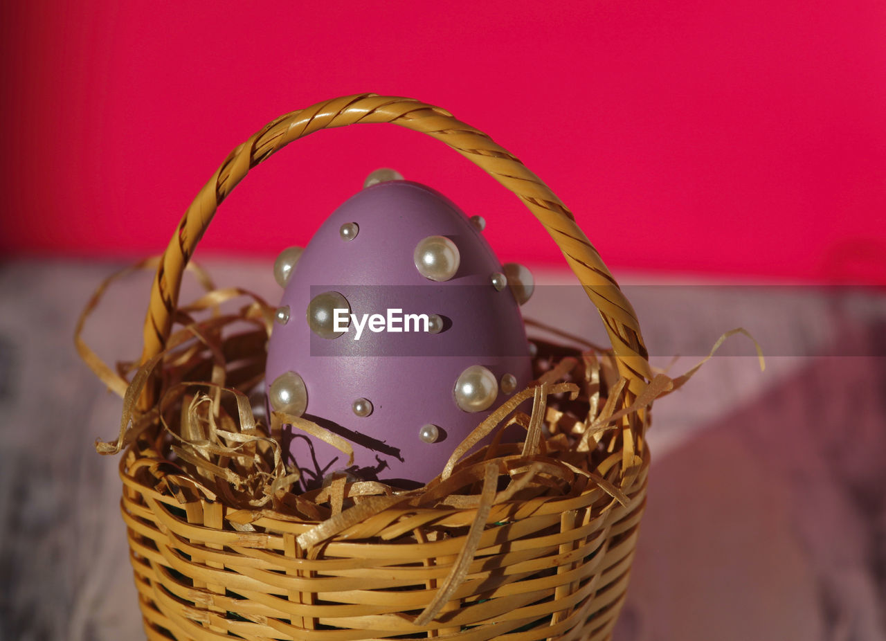Homemade purple easter egg in easter basket 
on white table with pink background