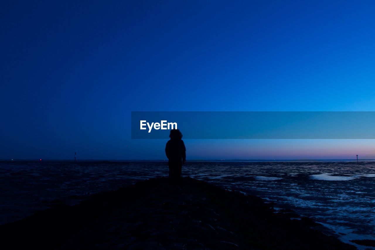 SILHOUETTE WOMAN STANDING ON BEACH AGAINST CLEAR BLUE SKY