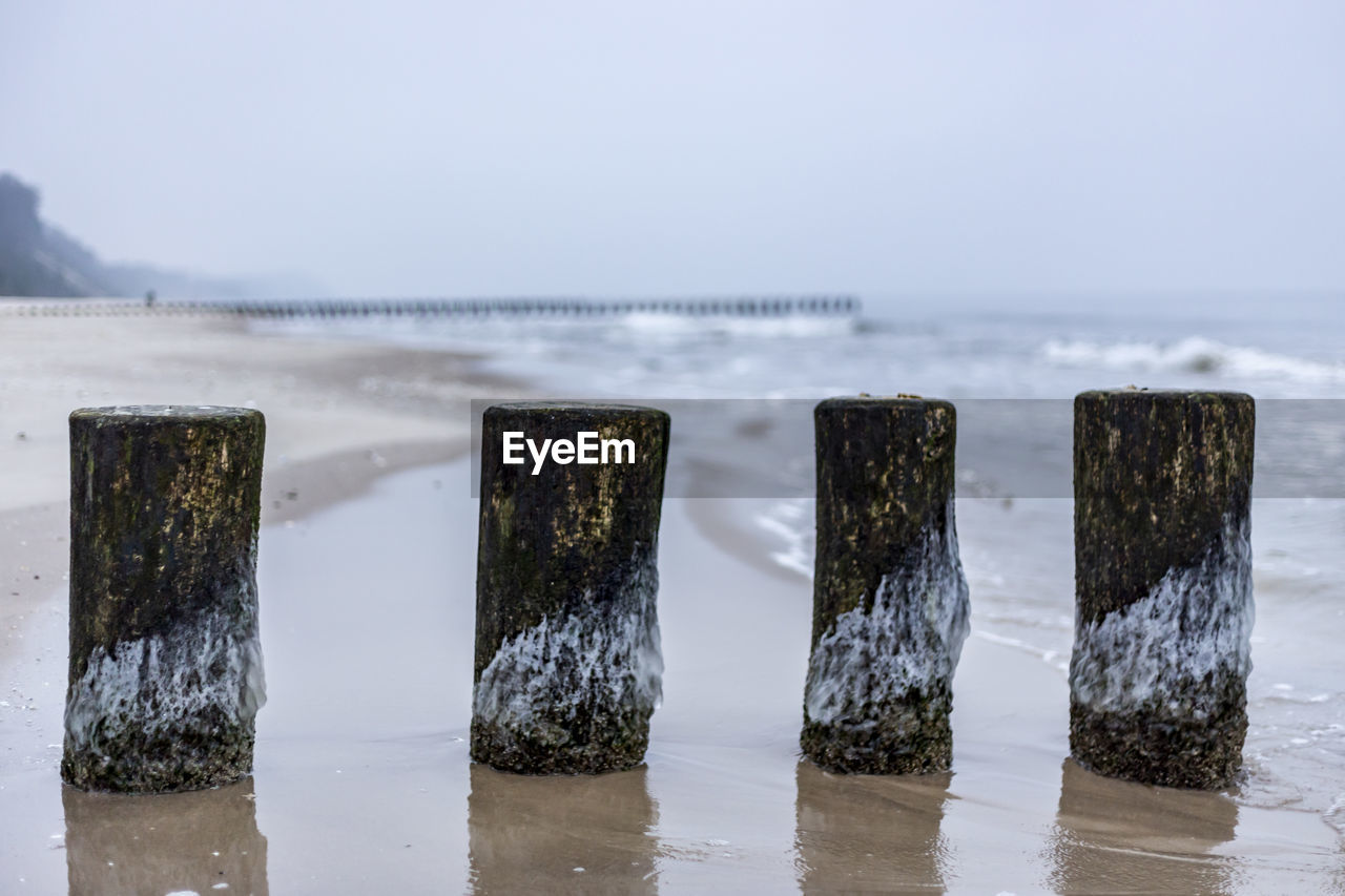 WOODEN POSTS ON SEA AGAINST SKY