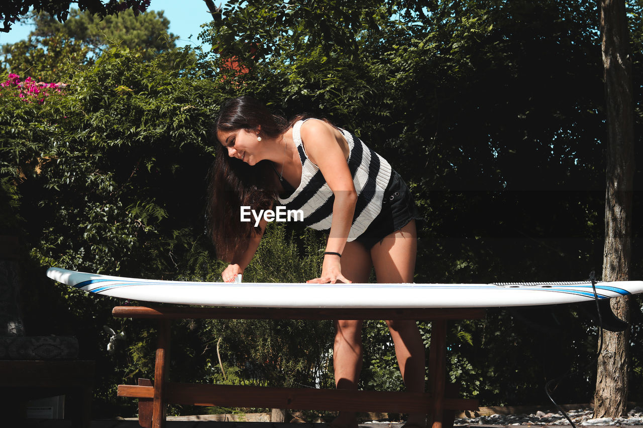 Woman by surfboard against trees