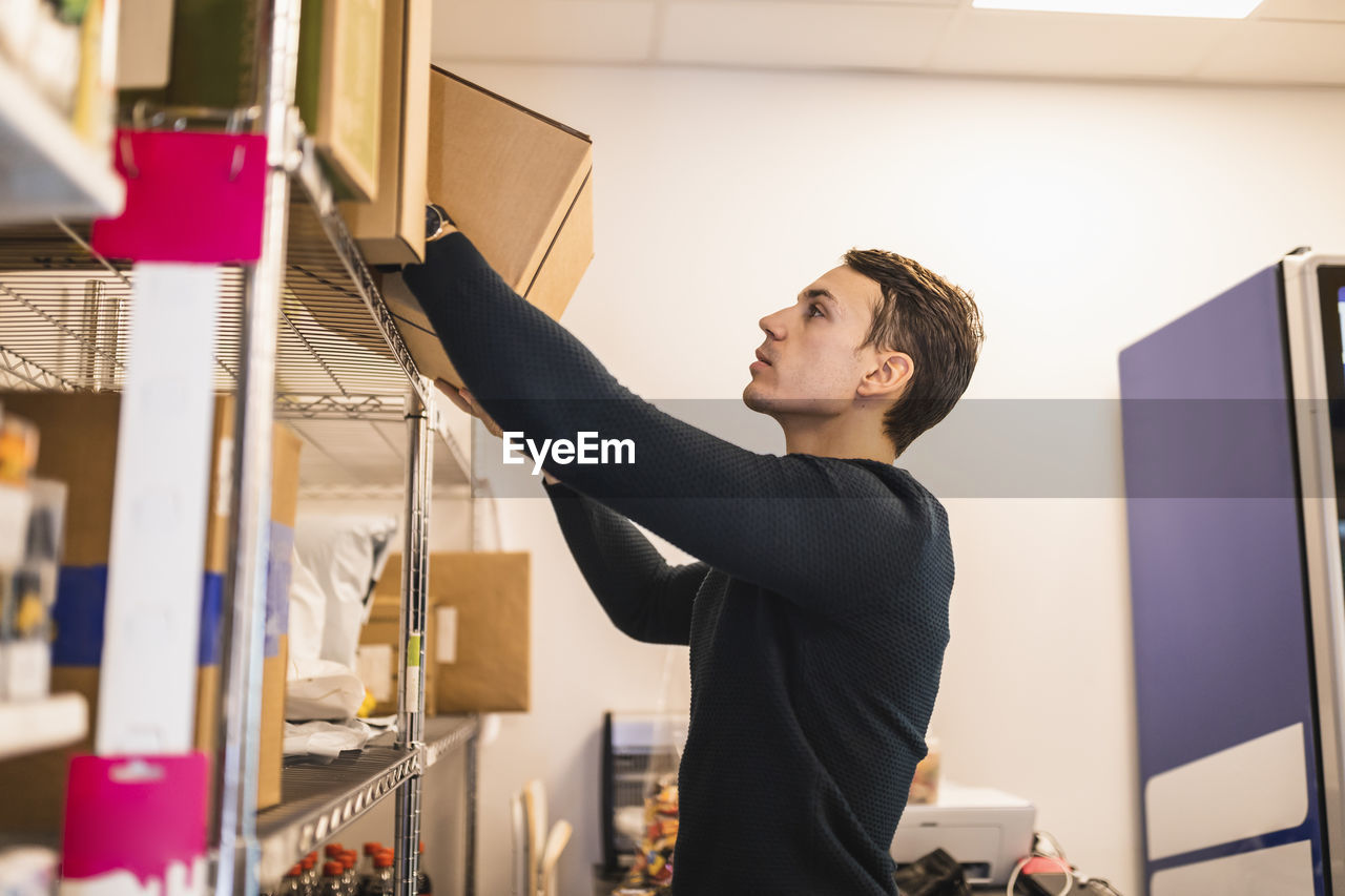 Male store owner removing box from shelf while working