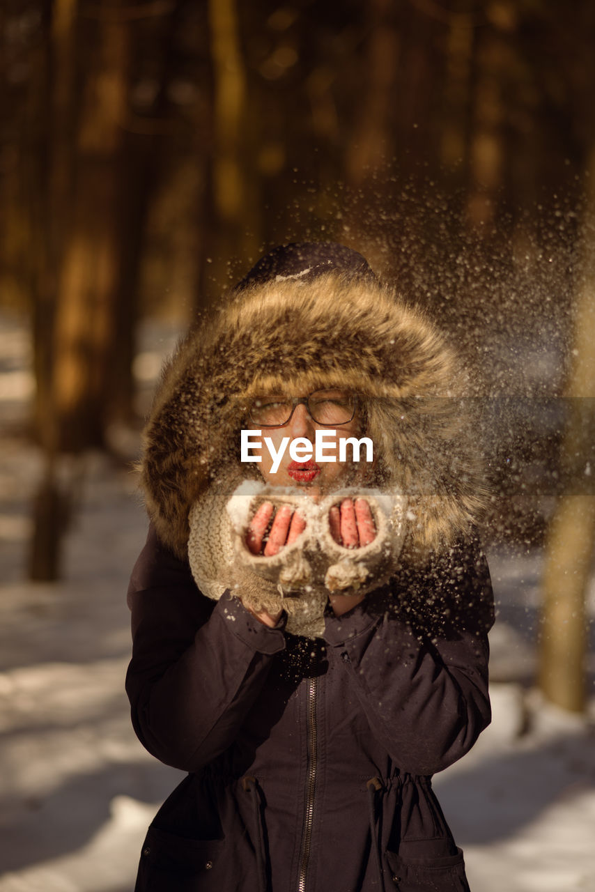 Portrait of young woman blowing snow on field