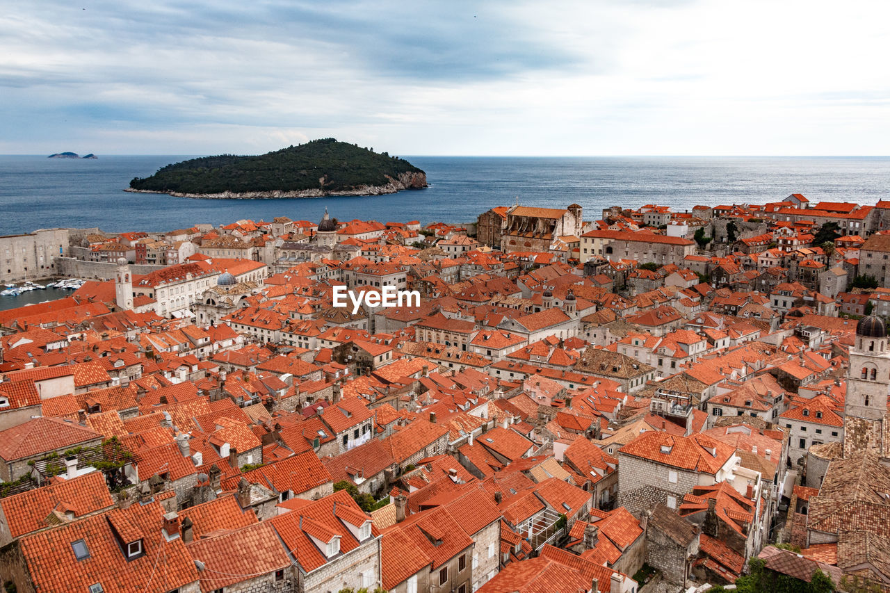 High angle view of townscape by sea against cloudy sky