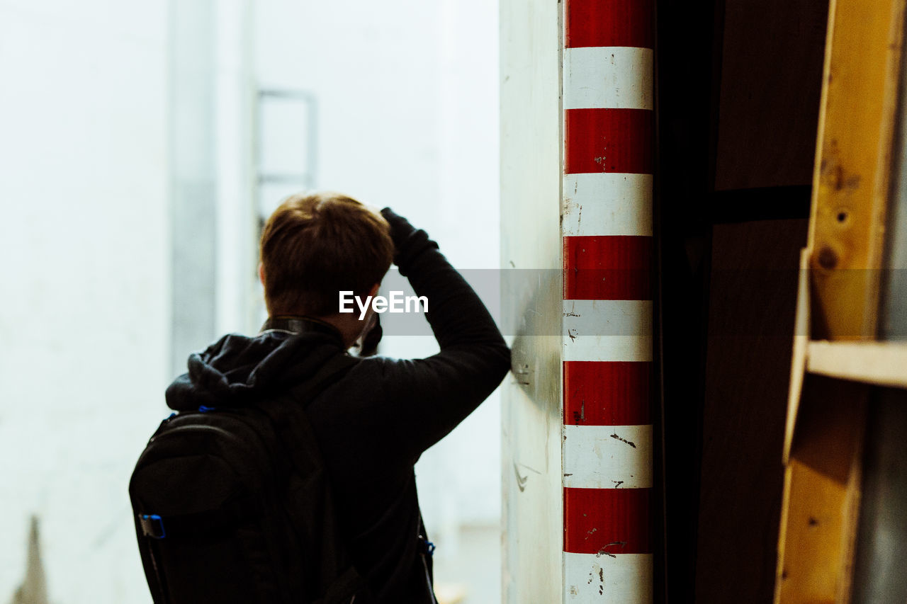 Rear view of man wearing backpack while standing by wall