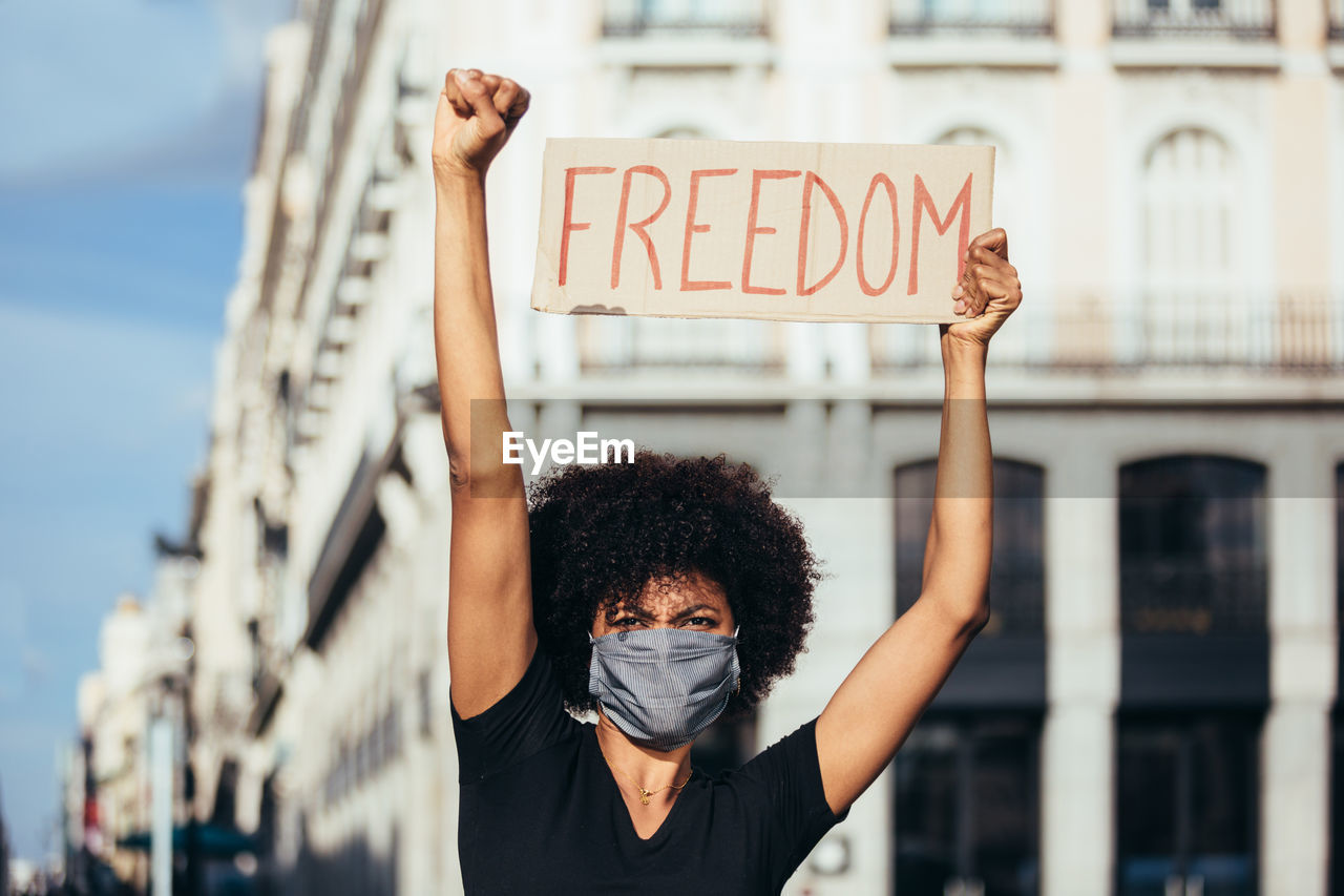 Afro woman protesting at a rally for racial equality. she is raising fist holding a sign with the word "freedom". black lives matter.