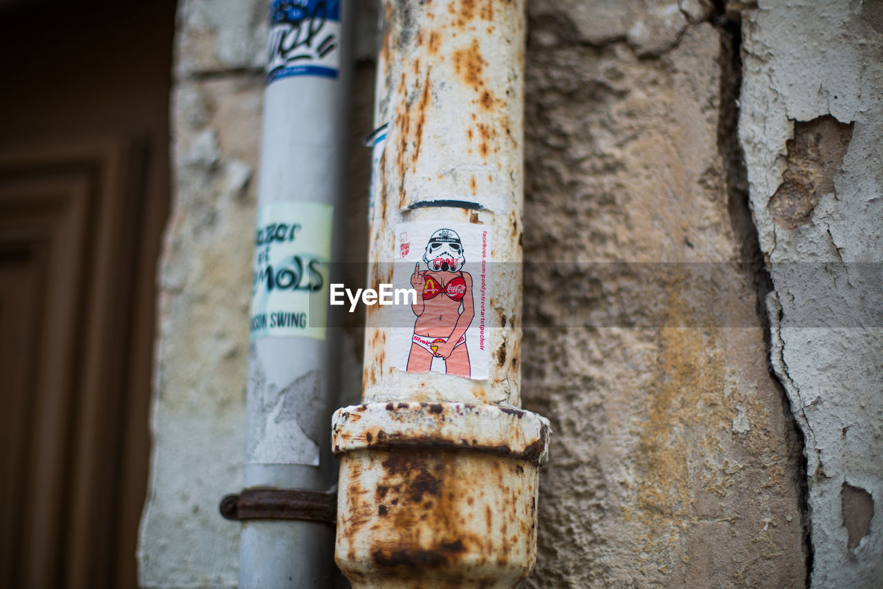 Sticker showing obscene gesture on rusty metallic pipe against wall