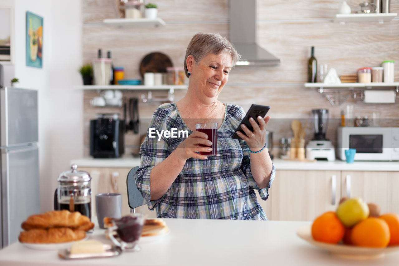 Senior woman holding mobile phone at kitchen