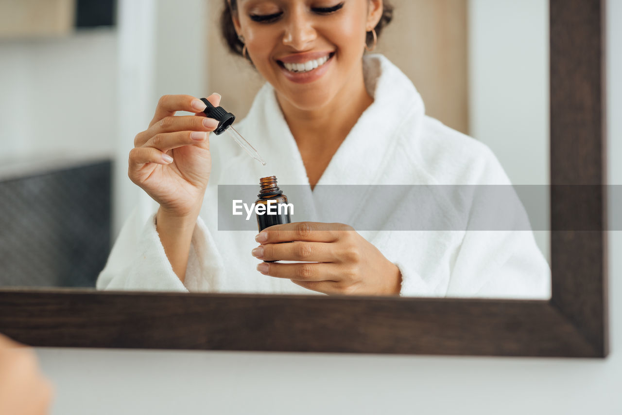 Reflection of smiling woman holding bottle seen in mirror