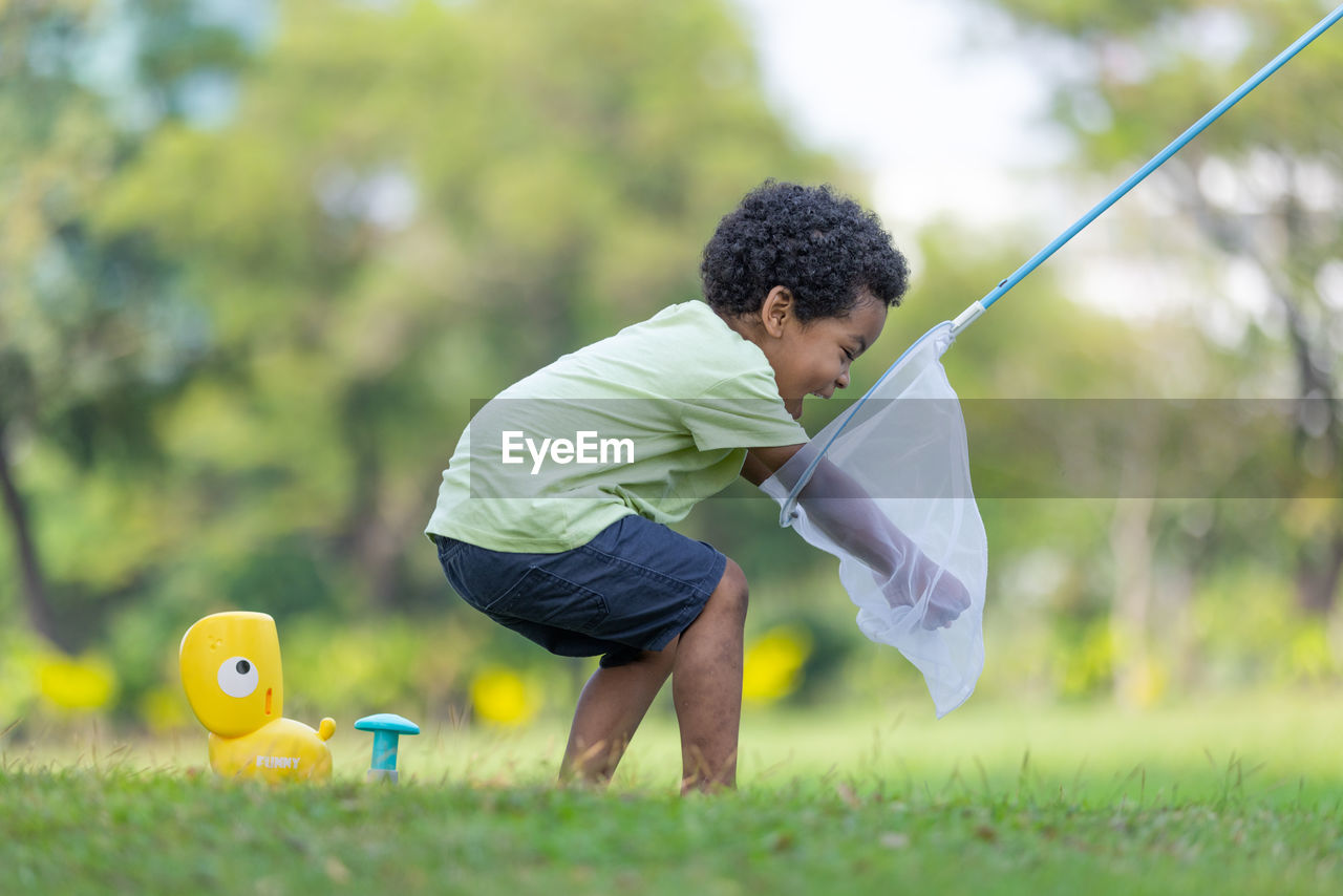 side view of boy playing with arms raised standing on field