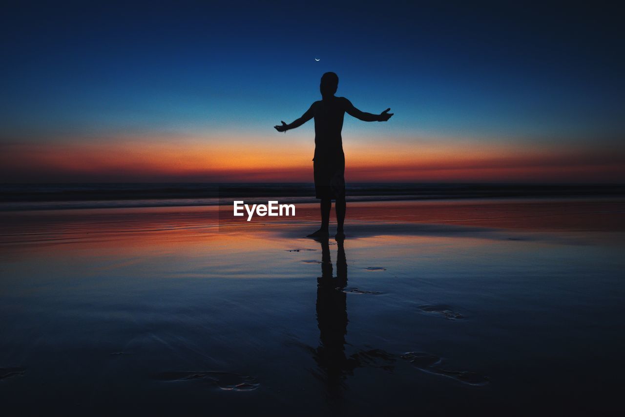 Silhouette of man standing on beach with arms outstretched