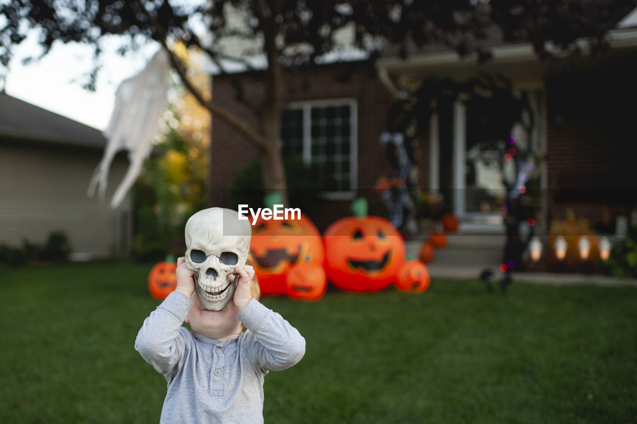 Toddler holding skeleton head in front of halloween decorations