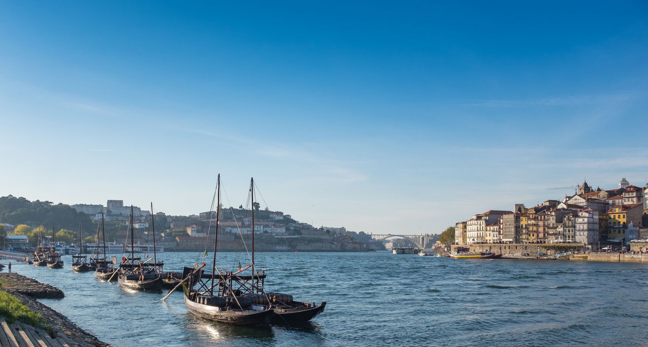 SAILBOATS MOORED ON SEA BY BUILDINGS AGAINST SKY