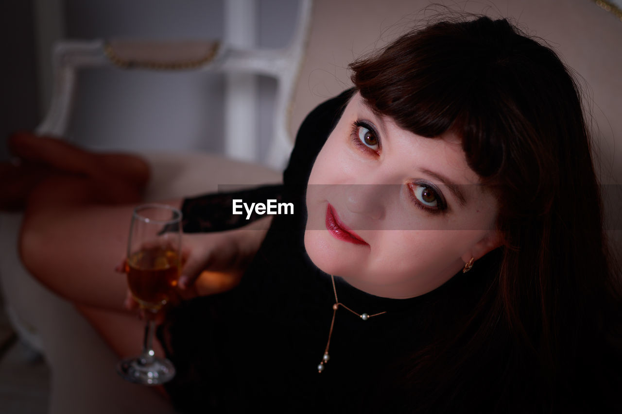 Close-up portrait of mature woman holding wineglass while sitting at home