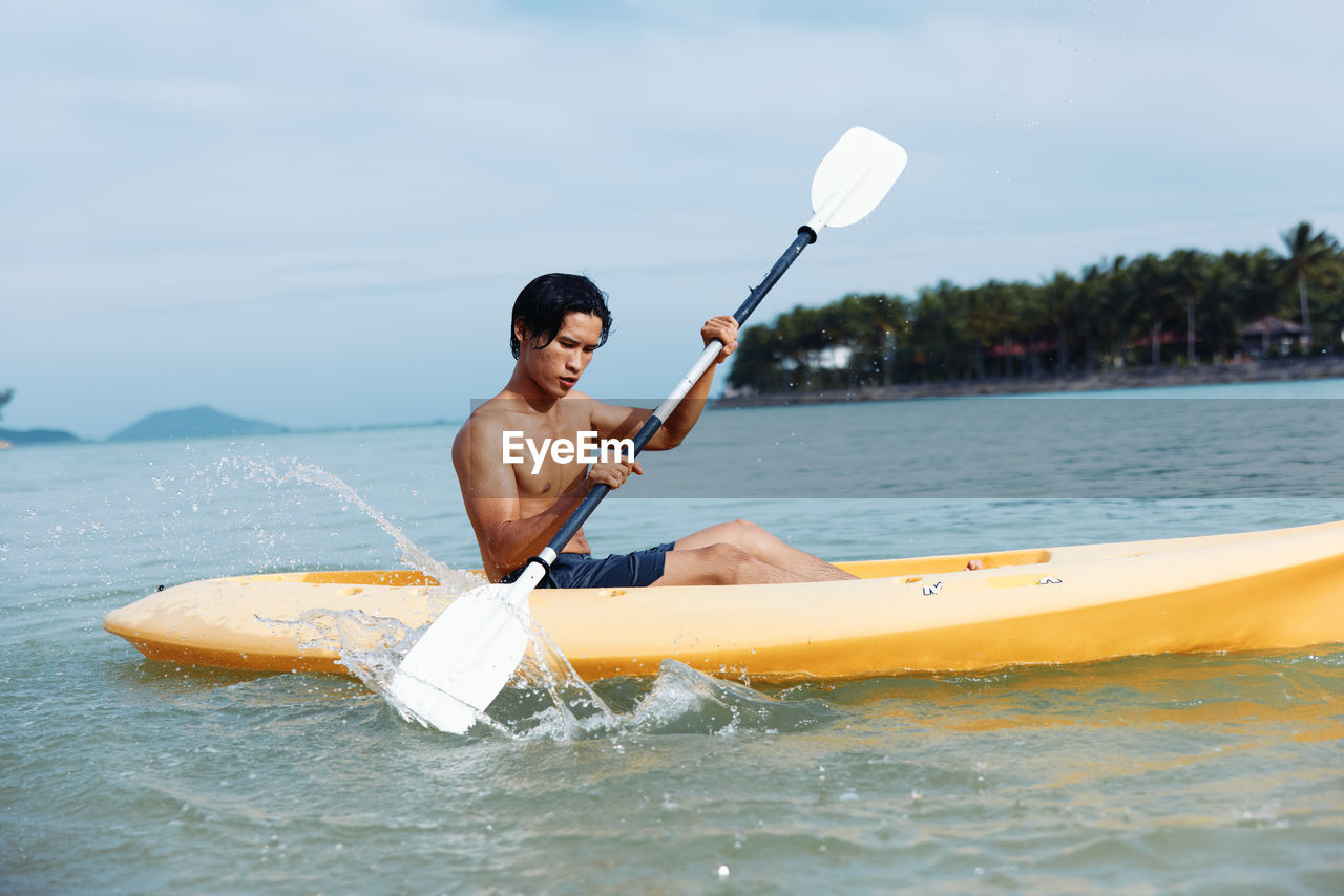 portrait of man kayaking in sea against sky