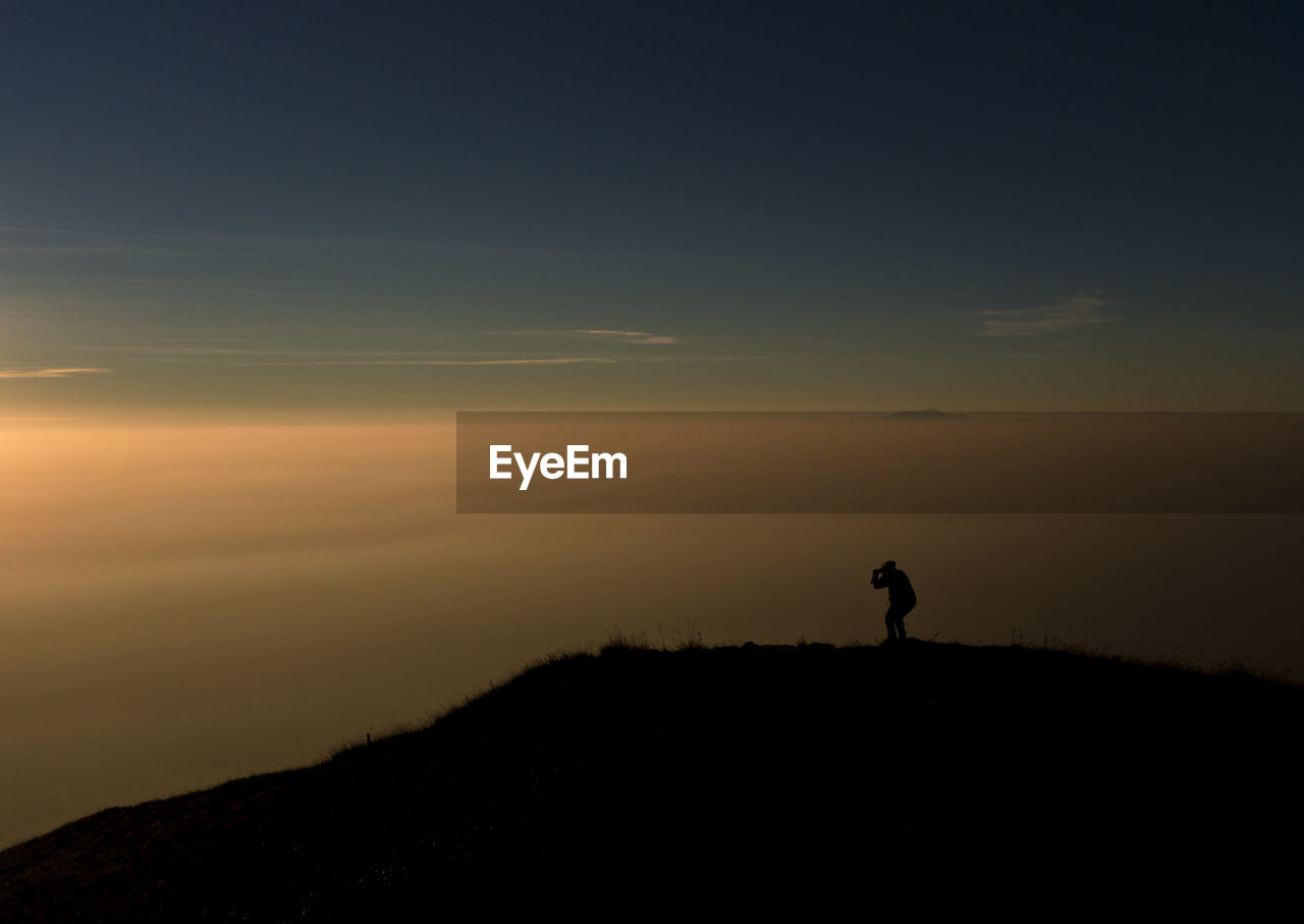 Silhouette man standing on mountain against sky during sunset