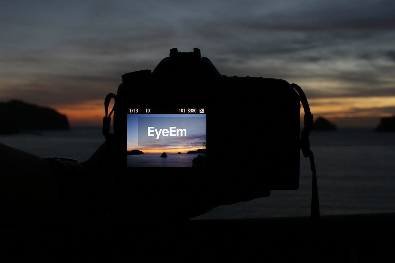 CLOSE-UP OF SILHOUETTE CAMERA ON BEACH AGAINST SKY