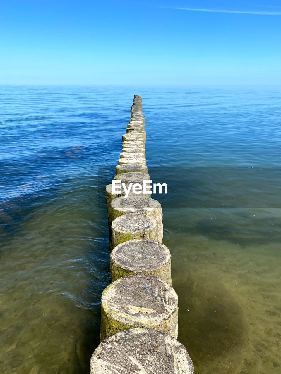 STACK OF WOODEN POST IN SEA AGAINST SKY