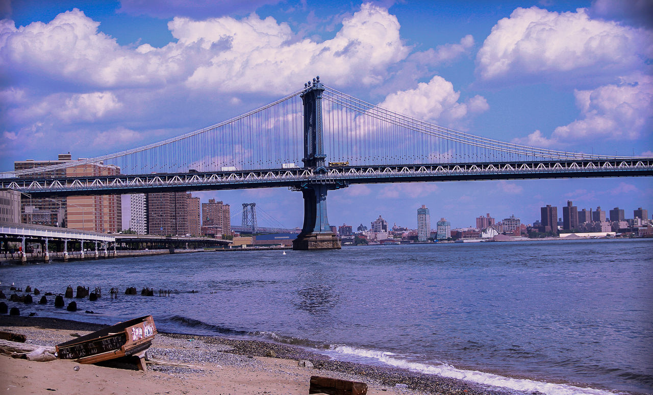 Old abandoned piano by manhattan bridge and river against cloudy sky in city