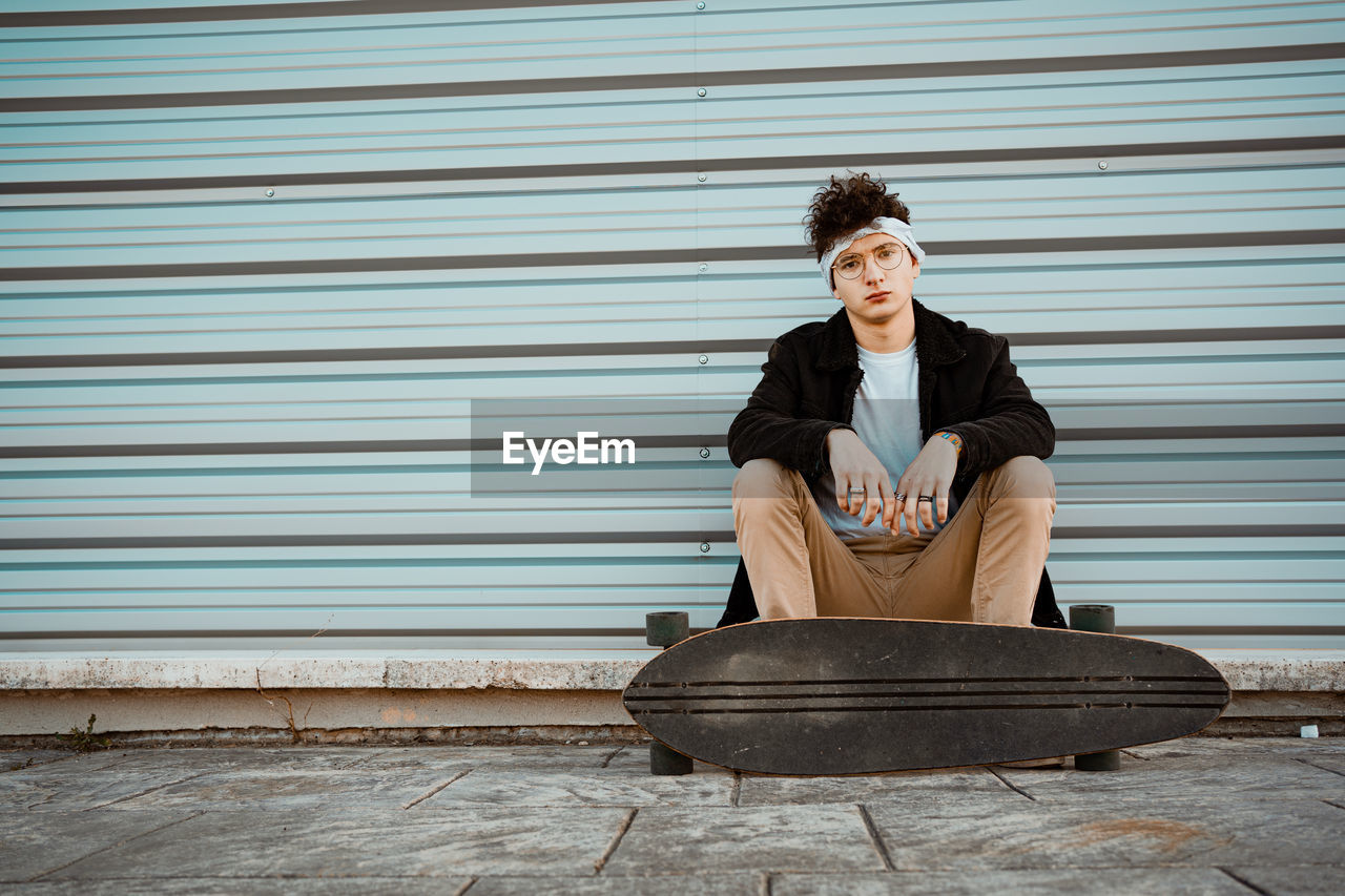 PORTRAIT OF YOUNG MAN SITTING ON METAL WALL