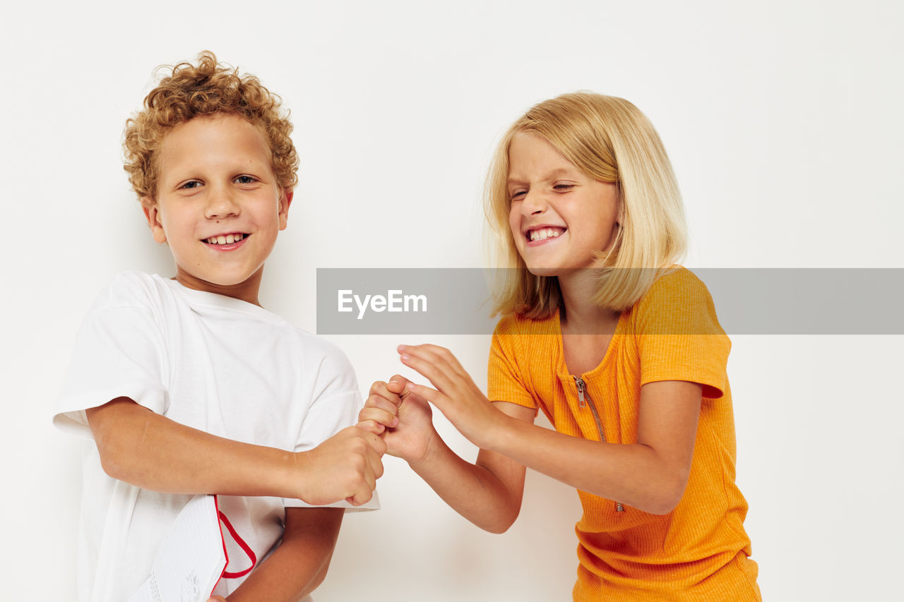 Portrait of smiling sibling playing against white background