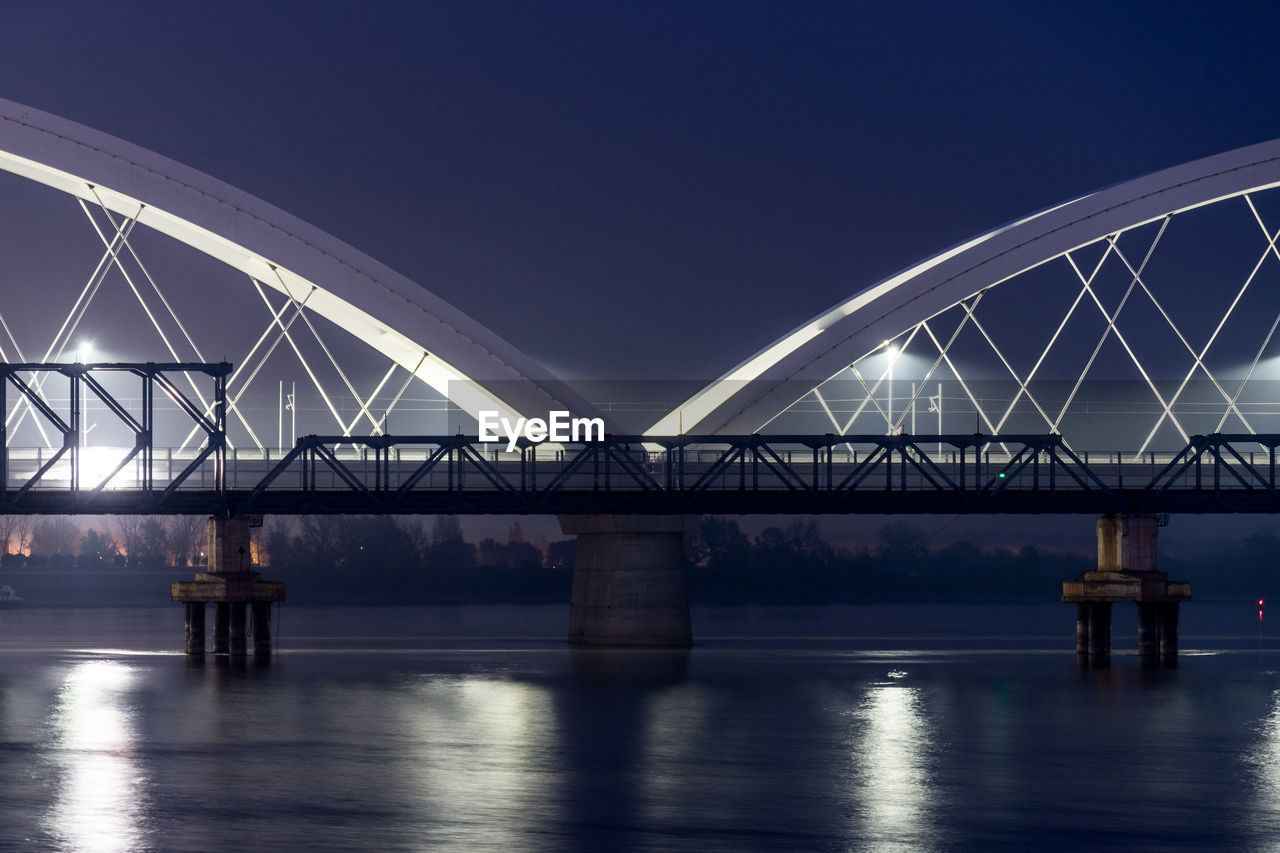 Illuminated bridge over river against clear sky at night