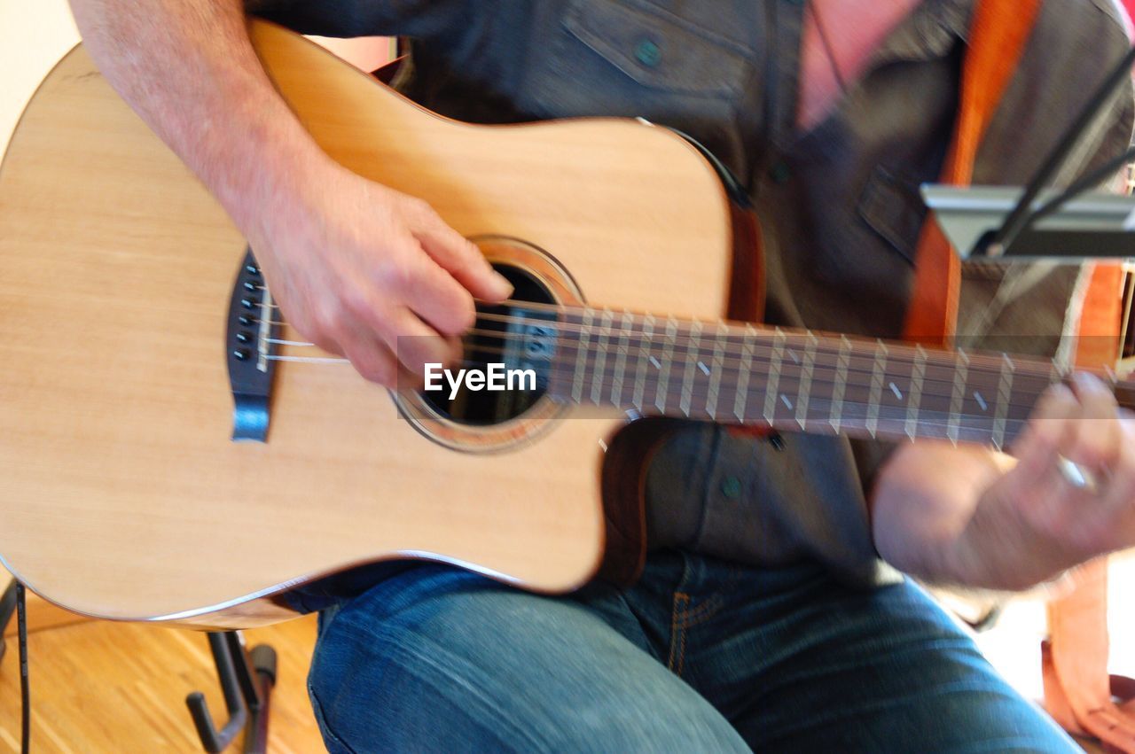 MIDSECTION OF MAN PLAYING GUITAR IN BEDROOM