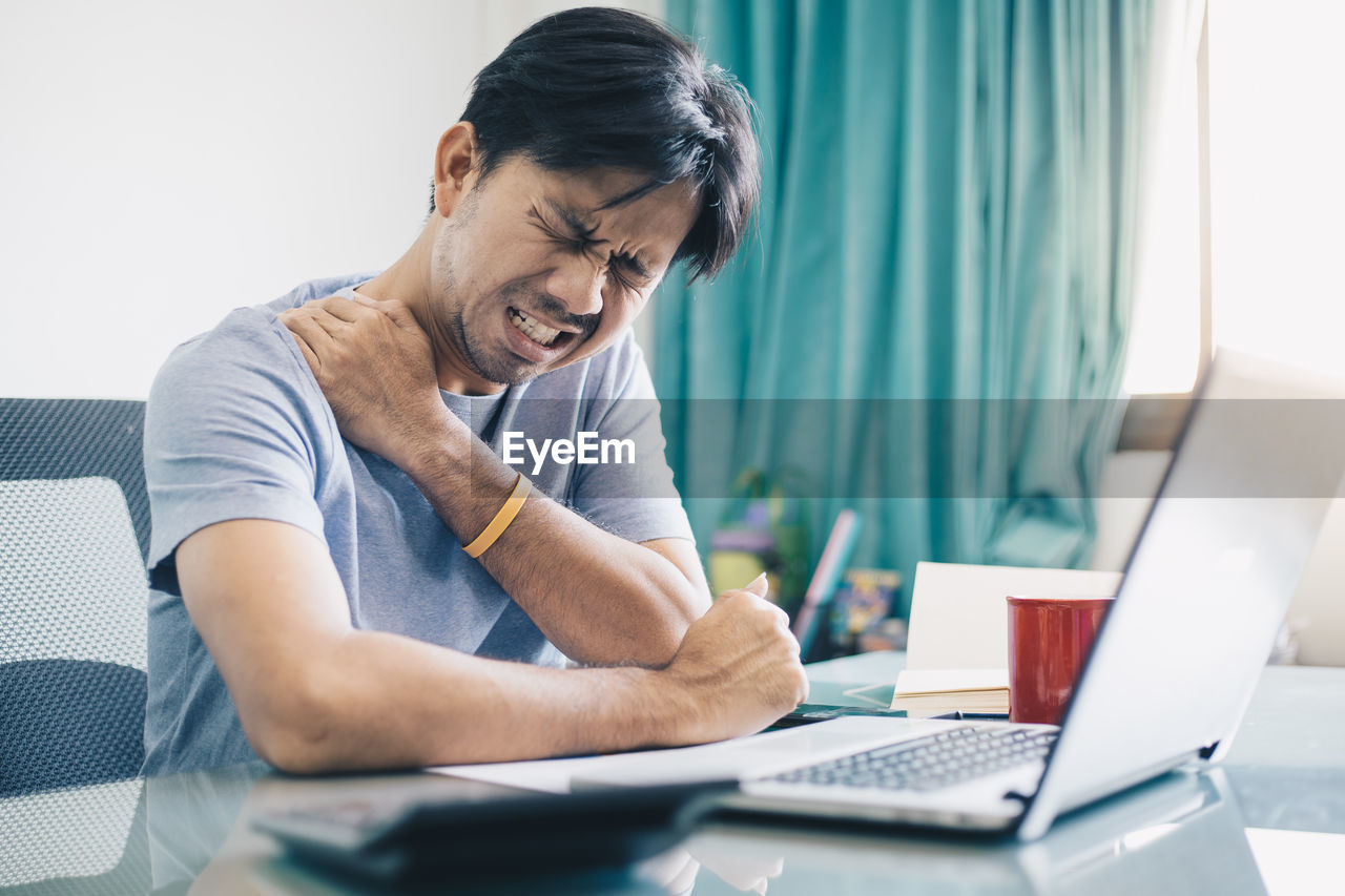 REAR VIEW OF MAN WORKING WITH LAPTOP