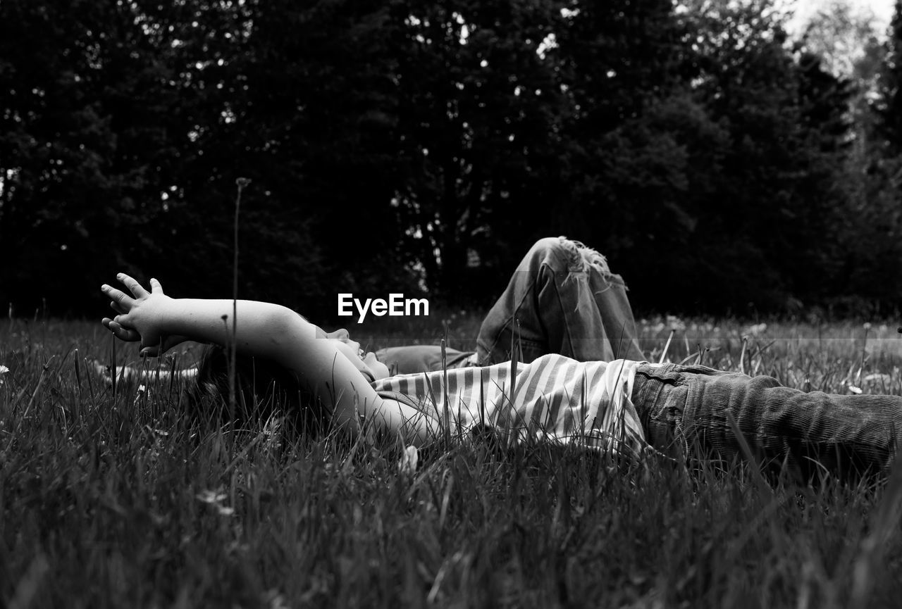 Siblings lying down on field against trees