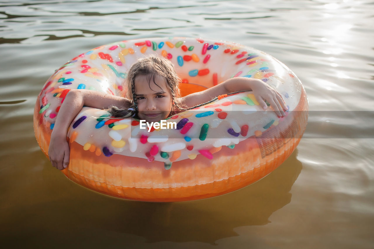 Girl swims with big donut inflatable ring on lake on hot summer day, happy summertime, cottagecore