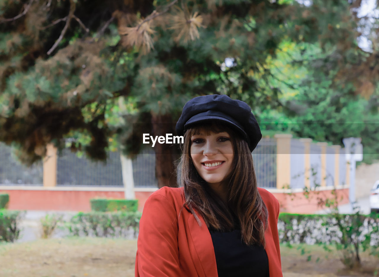 PORTRAIT OF SMILING WOMAN STANDING AGAINST PLANTS