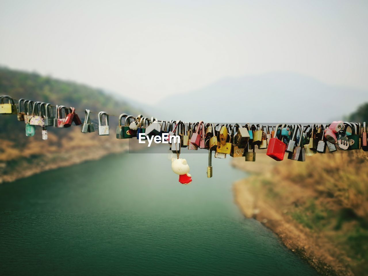 Padlocks hanging on bridge over river against sky